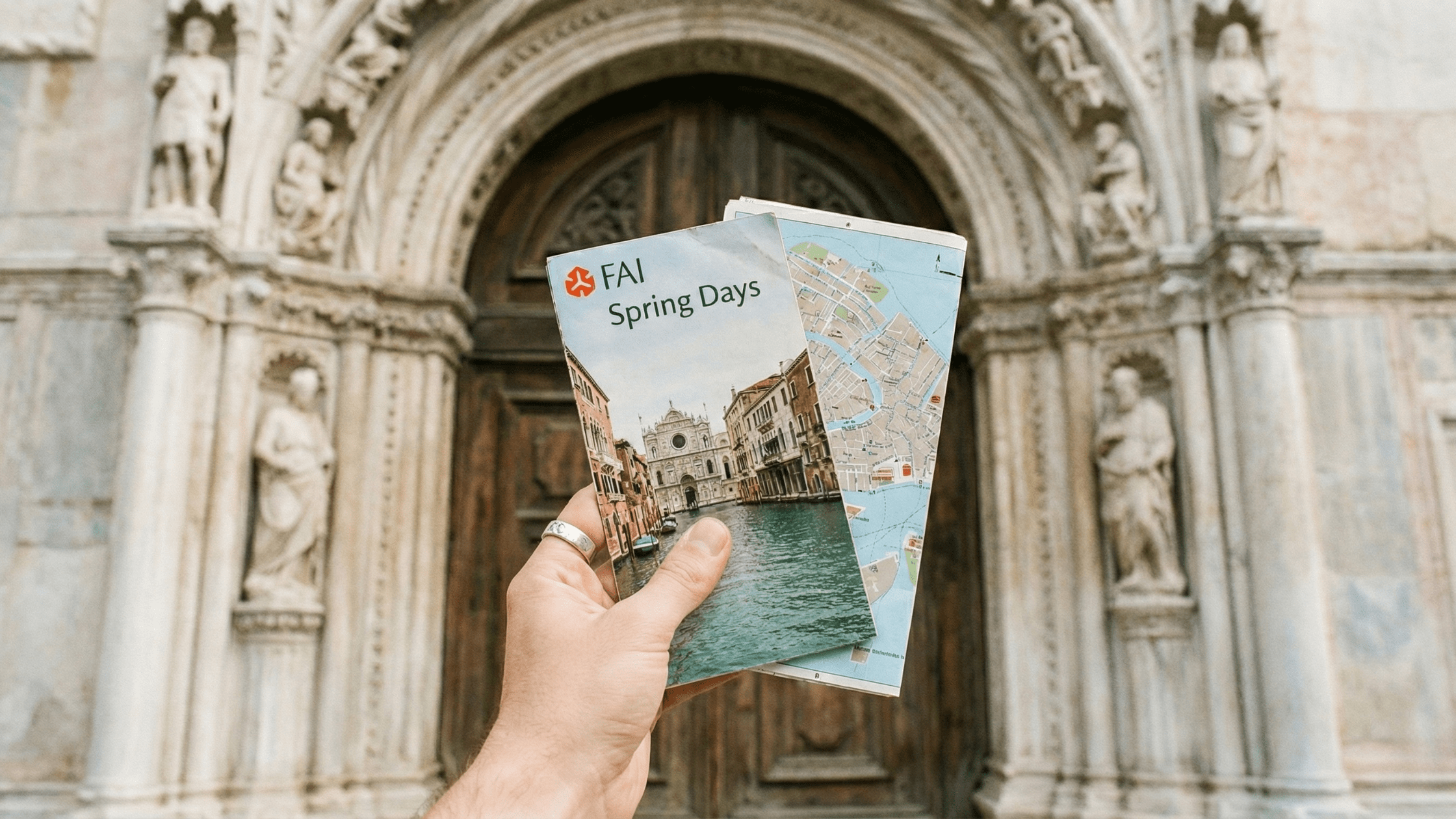 Dettaglio di un viaggiatore con brochure FAI e mappa di Venezia davanti all'ingresso monumentale di un palazzo storico.